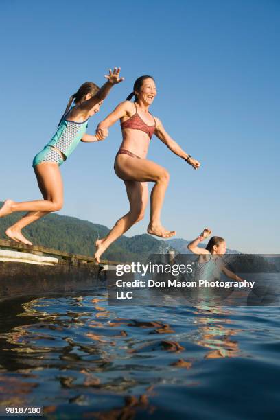 mother and daughters jumping into lake - asian woman swimsuit stock-fotos und bilder