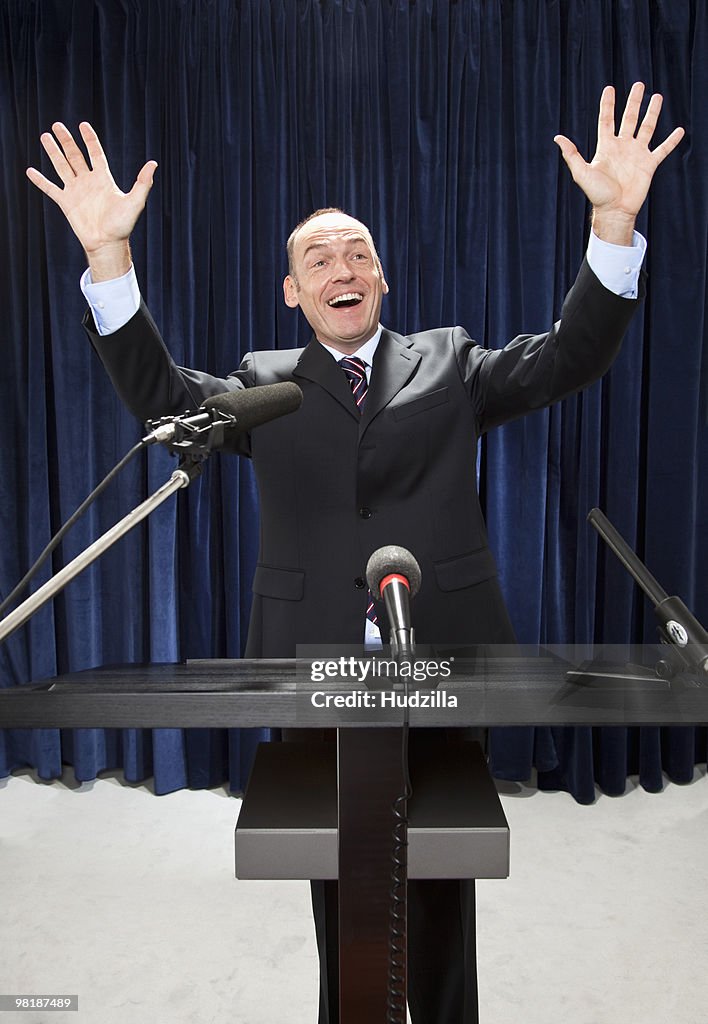 A man in a suit gesturing at a lectern