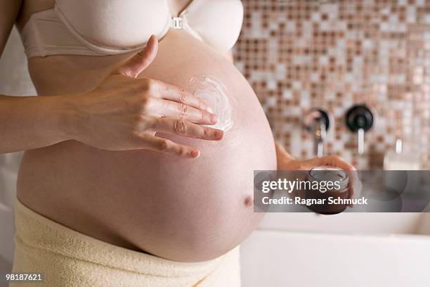 a pregnant woman rubbing moisturizer on her belly, midsection - body photos et images de collection