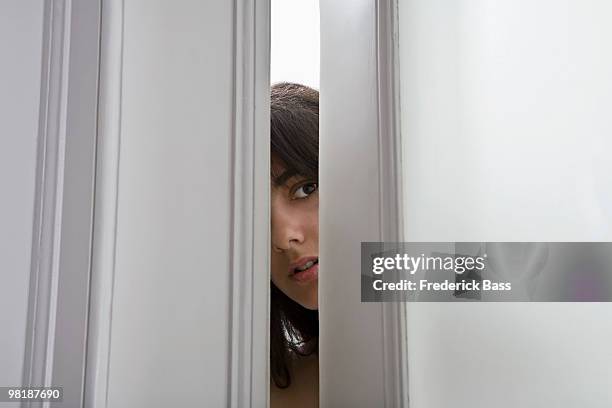 a woman peeking through a cracked door - door ajar stock pictures, royalty-free photos & images