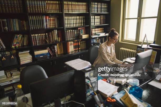 young woman with eyeglasses typing on a computer in the library - librarian stock pictures, royalty-free photos & images