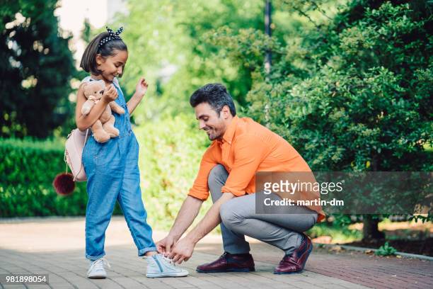 smiling father tying shoelaces of her daughter in the park - tieing shoelace stock pictures, royalty-free photos & images