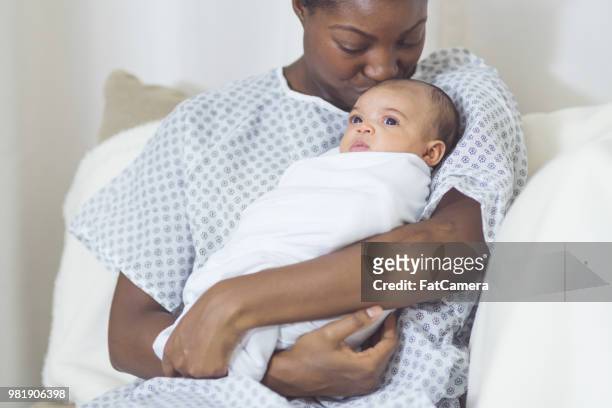hermosa madre afroamericana en una bata de hospital tiene a su bebé recién nacido suavemente a su pecho - hospital gown fotografías e imágenes de stock