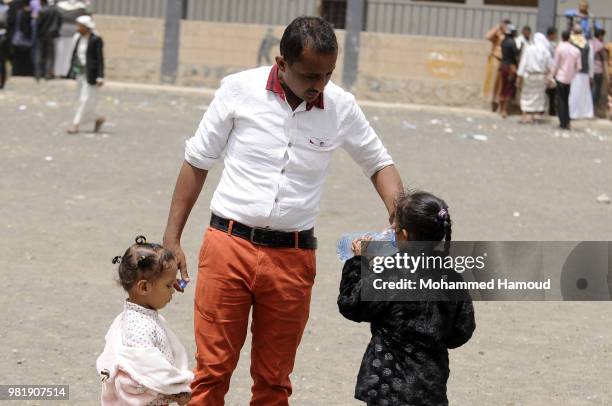 Yemeni displaced man gives his child water as they wait to register their names in order to obtain a shelter after they fled their homes during...