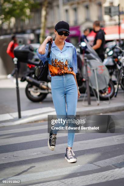 Guest wears a cap, sunglasses, a colored shirt, blue pants, sneakers, outside CDG Comme des Garcons, during Paris Fashion Week - Menswear...