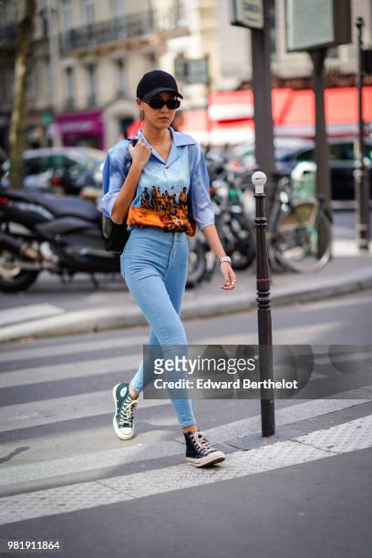 Guest wears a cap, sunglasses, a colored shirt, blue pants, sneakers, outside CDG Comme des Garcons, during Paris Fashion Week - Menswear...