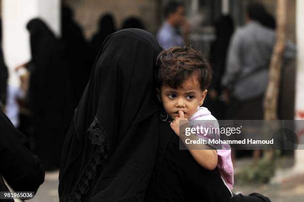 Yemeni displaced woman carries her daughter as she waits to register register in order to obtain a shelter after they fleeing during fighting and...