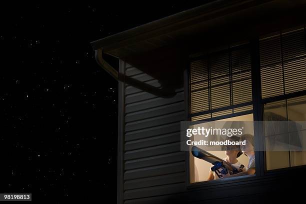 teenage boys stand with telescope at open window looking at night sky - telescopio astronómico fotografías e imágenes de stock