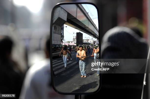 Flagellants are reflected in the wing mirror of a car as they flog themselves during a march to Malacanang palace in Manila on March 30, 2010. Roman...