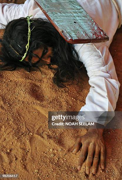 An Indian Catholic man dressed as Jesus Christ and carrying a cross lies in the dirt during a 'passion play' tableau on Good Friday at Mount Carmel...