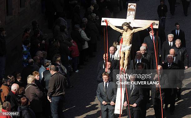 Believers stand on the side and waitch men carrying a cross with a likeness of Jesus Christ during a Good Friday procession to commemorate the death...