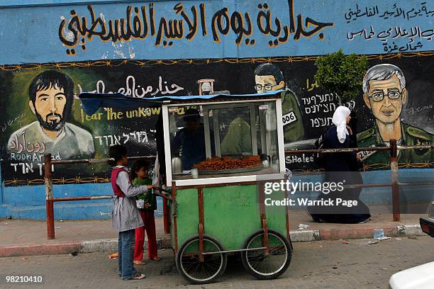 Palestinian children purchase food from a street vendor next to a Hamas police station adorned with paintings of abducted Israeli solider, Gilad...