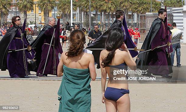 Beachgoers watch as people taking part in the "Cristo Salvador y del Amparo " brotherhood procession pass by on Good Friday on a beach in Valencia on...