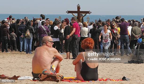 Beachgoers watch as people taking part in the "Cristo Salvador y del Amparo " brotherhood procession pass by on Good Friday on a beach in Valencia on...