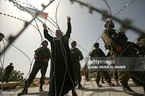 Israeli soldiers stand guard as a Palestinian woman waves her national flag during a demonstration against Israel's controversial separation barrier...