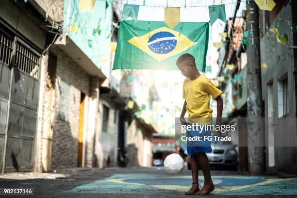 niño brasileño jugando al fútbol en la calle - brasileño fotografías e imágenes de stock