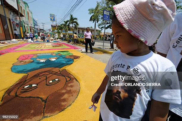 Child wearing a Jesus Christ t-shirt looks at a carpet made out of coloured sand on the street ahead of the Good Friday procession, in Santa Barbara,...