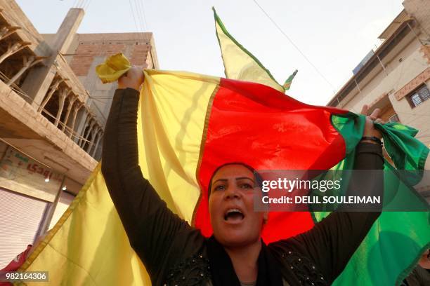 Syrian-Kurdish woman waves a Kurdish flag as she protests against demographic changes forced by Turkey to repopulate Kurdish areas, in Qamishli on...