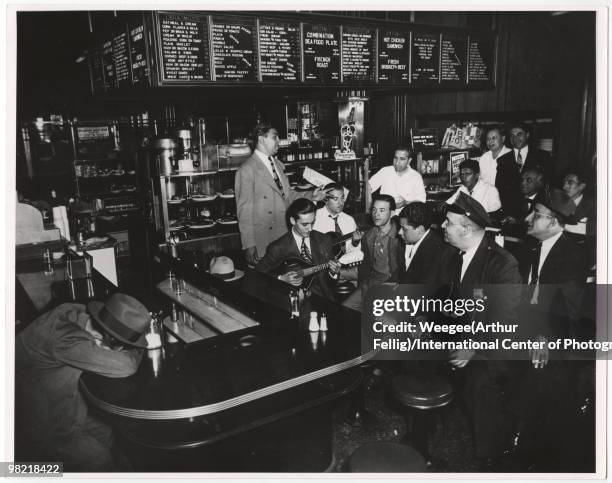 Musicians play instruments, guitar and mandolin, and a man sings inside a cafeteria, while people, including a police officer, listen, New York,...