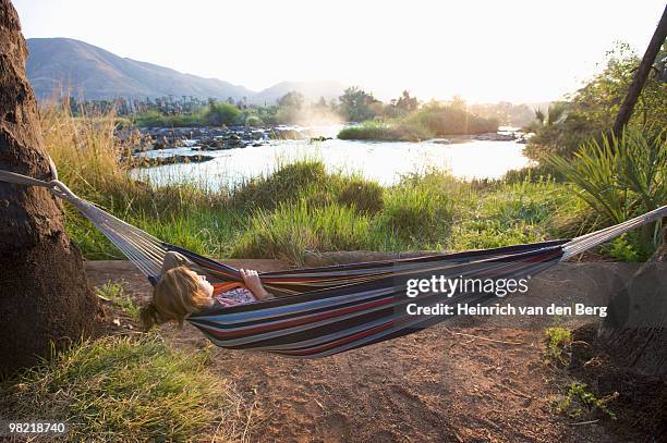 young woman sleeping in a hammock next to epupa falls, kunene river, kaokoland, namibia - freek van den bergh stock pictures, royalty-free photos & images