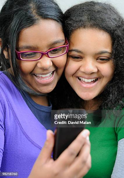 teenage girls laughing while looking at mobile phone, cape town, western cape province, south africa - wange an wange stock-fotos und bilder