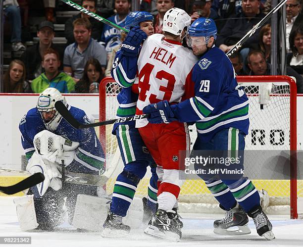 Roberto Luongo of the Vancouver Canucks makes a save as Aaron Rome and Kevin Bieksa of the Vancouver Canucks keep Darren Helm of the Detroit Red...