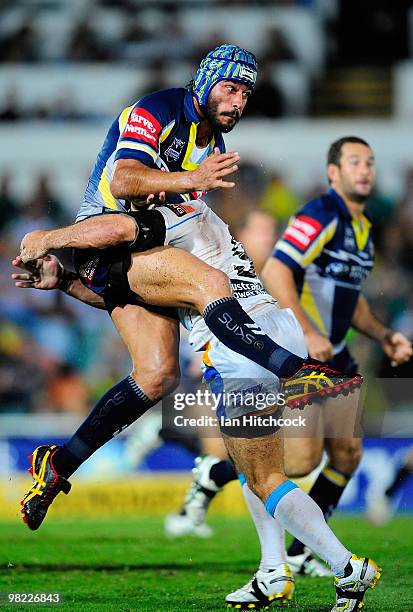 Johnathan Thurston of the Cowboys gets a kick away despite the tackle of Nathan Friend of the Titans during the round four NRL match between the...