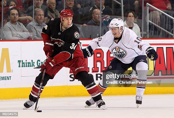 Daniel Winnik of the Phoenix Coyotes skates with the puck under pressure from Shawn Horcoff of the Edmonton Oilers during the NHL game at Jobing.com...