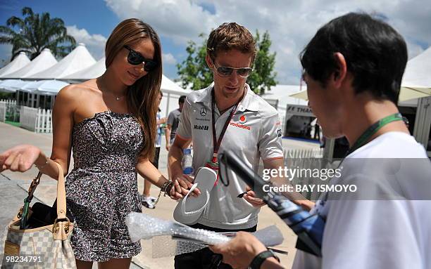 McLaren-Mercedes driver Jenson Button of Britain gives an autograph to a fan while walking with his girlfriend Jessica Michibata on prior to the...