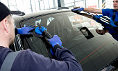 Automobile special workers replacing windscreen or windshield of a car in auto service station garage.