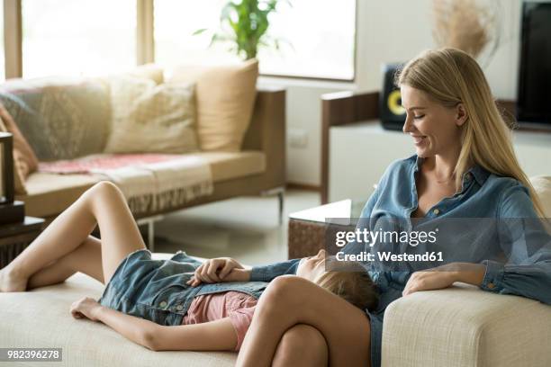 happy mother and daughter cuddling and relaxing on a couch in a modern living room - wealthy family inside home stock pictures, royalty-free photos & images