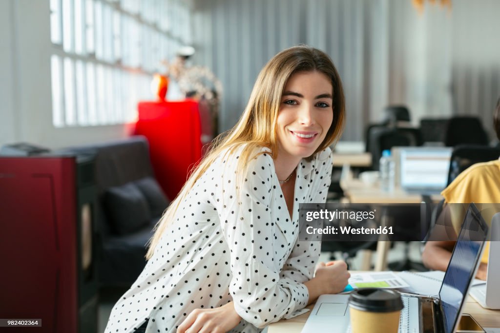 Portrait of smiling young woman at desk in office