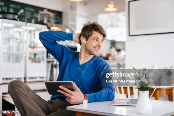 smiling man in a cafe with earphone, laptop and tablet - in ear headphones stock pictures, royalty-free photos & images