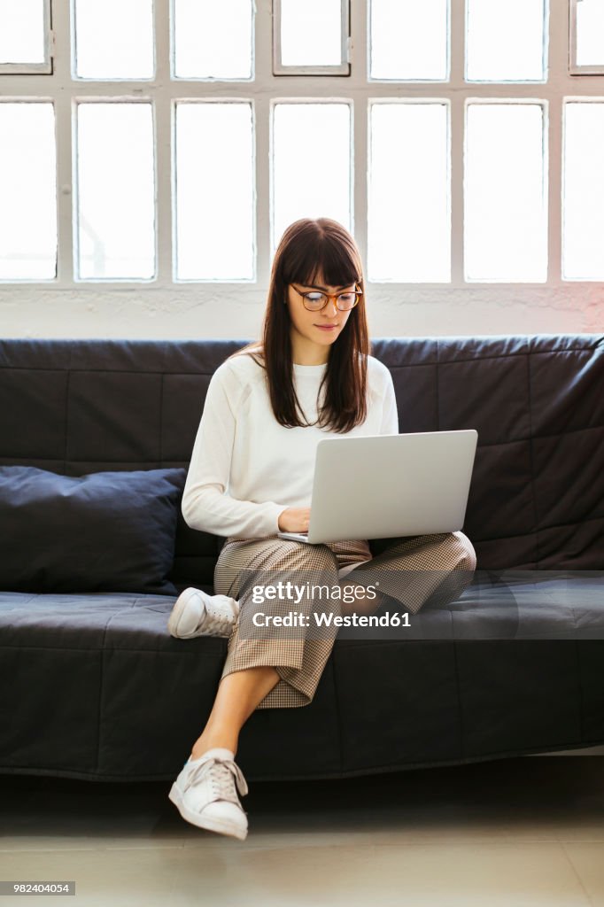 Young woman sitting on couch in office using laptop