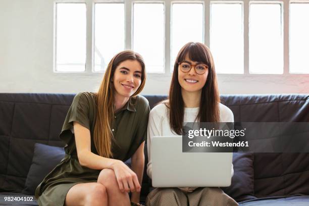 two smiling young women sitting on couch in office with laptop - smile close up stock pictures, royalty-free photos & images