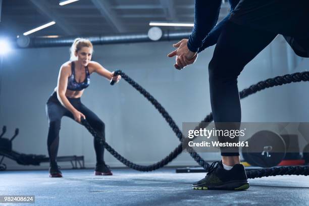 athletic woman doing battlerope exercise with personal trainer at gym - coaching stock-fotos und bilder