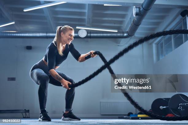 athletic woman exercising with battle ropes at gym - entrenamiento combinado fotografías e imágenes de stock