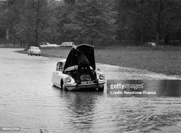 Suite à un gros orage, un conducteur est perché et penché sur le moteur de sa voiture arrêtée sur la chaussée inondée à Paris en France, le 5 mai...