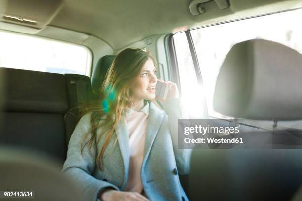 young businesswoman on the phone sitting on backseat of a car looking out of window - taxi españa stockfoto's en -beelden