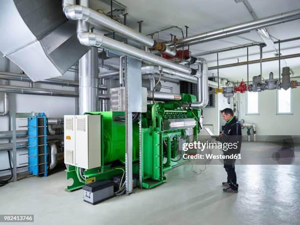 combined heat and power plant, worker using laptop in front of gas engine - generatore elettrico foto e immagini stock