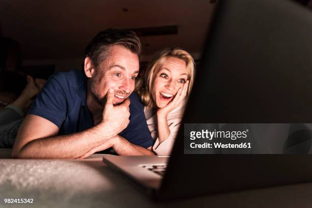 amazed mature couple lying on couch at home looking at laptop - mood stream stock pictures, royalty-free photos & images
