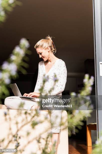 smiling mature woman sitting at open terrace door using laptop - open seat godo stock-fotos und bilder