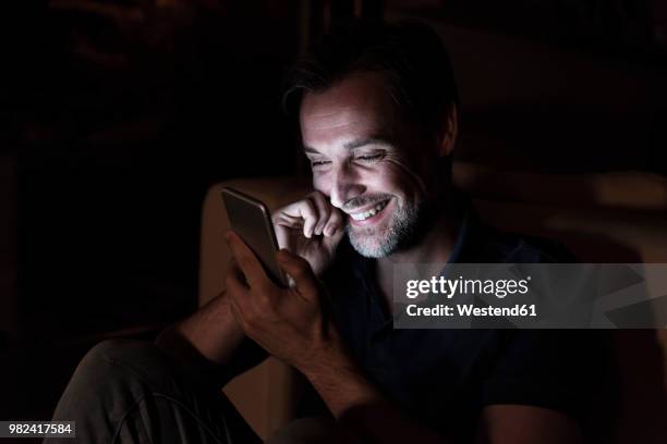 portrait of happy mature man using cell phone at home - kontrastreich stock-fotos und bilder