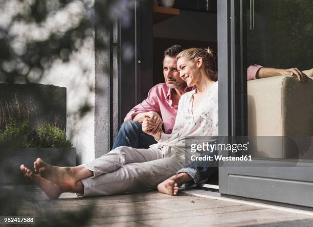 content mature couple relaxing together at open terrace door - at home stock-fotos und bilder