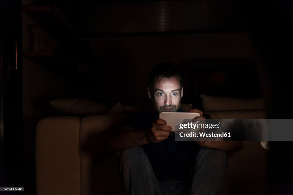 Man sitting in the dark at home starring at smartphone