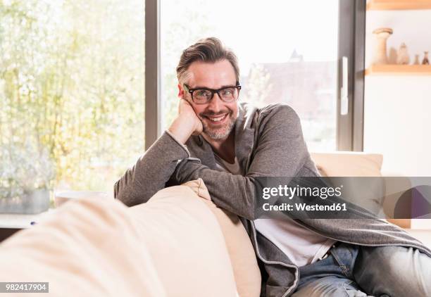 portrait of smiling man relaxing on couch at home - head in hands stock pictures, royalty-free photos & images
