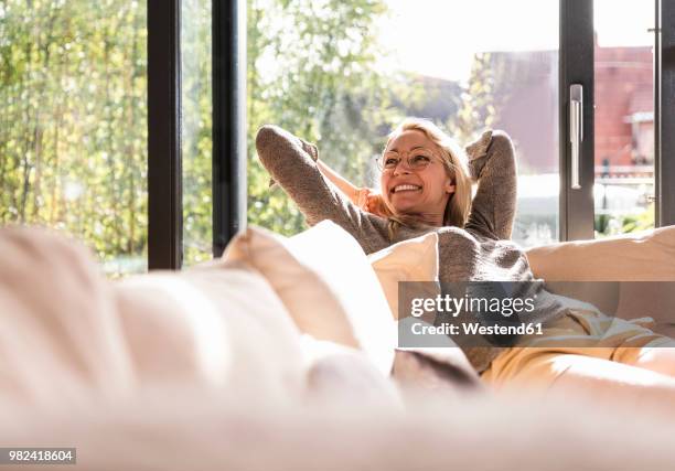 happy mature woman relaxing on the couch at home - bekväm bildbanksfoton och bilder