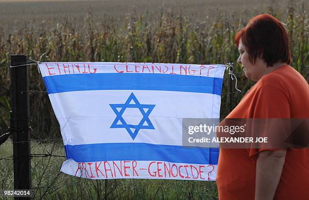 South African walks past an Israeli flag inscribed with the words "Ethnic Cleansing" and "Afrikaner-Genocide?" hung on the fence of farmer and far...