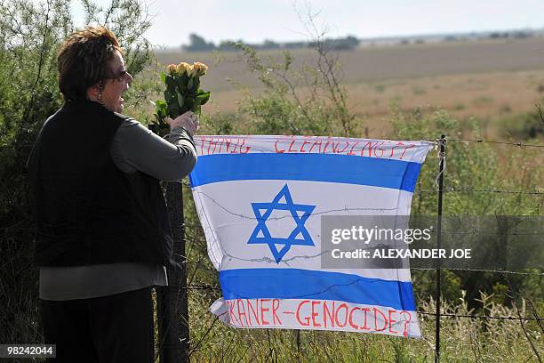 South African lays flowers near an Israeli flag inscribed with the words "Ethnic Cleansing" and "Afrikaner-Genocide?" hung on the fence of farmer and...