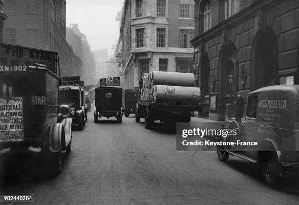Voitures publicitaires transportant les journaux et camion transportant des rouleaux de papier dans Fleet Street à Londres en Angleterre au...